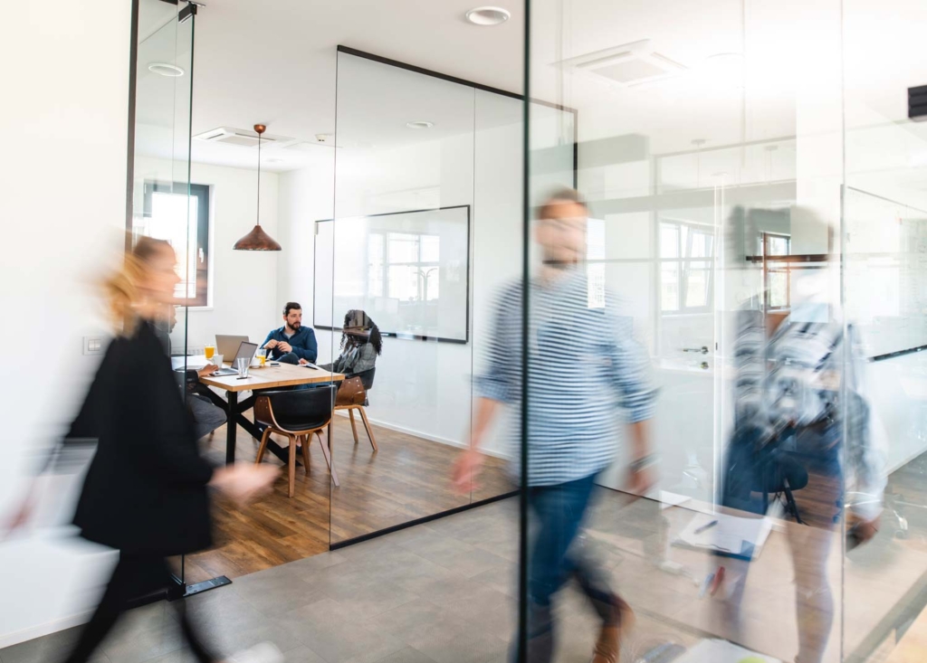 Tre individer som snabbt går förbi ett möte som pågår i bakgrunden