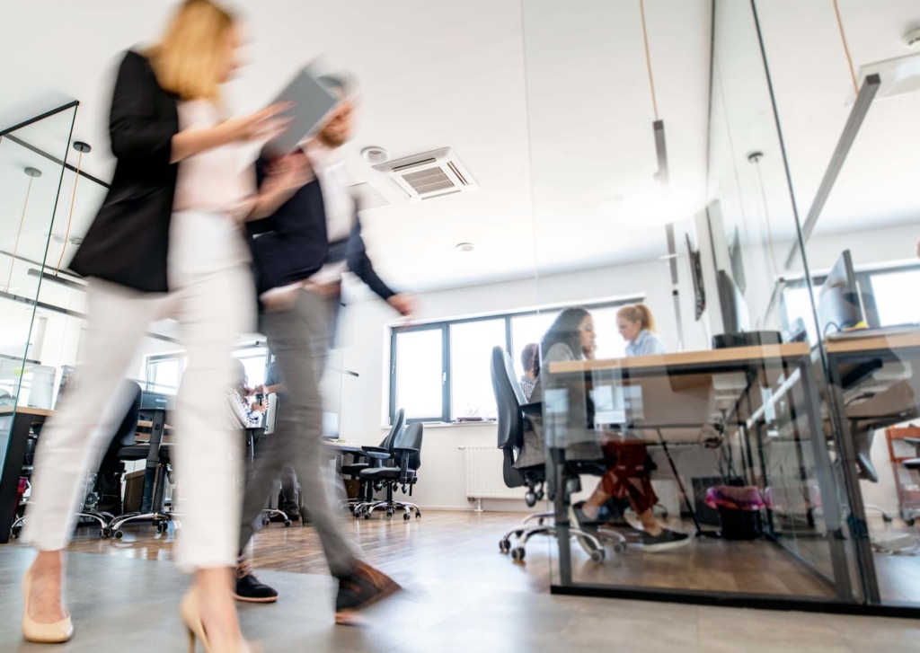 Två personer som snabbt går förbi ett öppet kontorslandskap